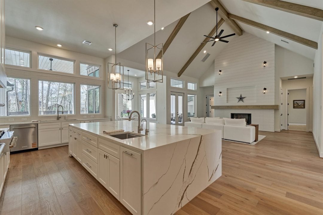 | the mckellar group Interior View of a Bright Modern Home from the Kitchen with Luxury Lighting Picture Windows a Quartz Waterfall Edge Island and Living Room with a Fireplace in the Background