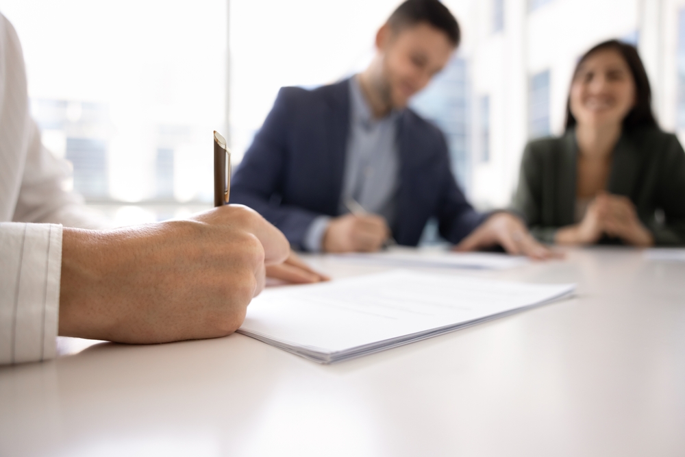 Businessmansigningcontractwithmalepartneronnegotiationmeetingusing | the mckellar group Closing Table for Real Estate Property in Conroe Texas