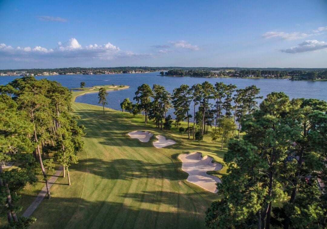 Aerial View of a Golf Course Along a Lake with Sand Bunkers and Tall Pines Lining the Fairways Under a Blue Sky