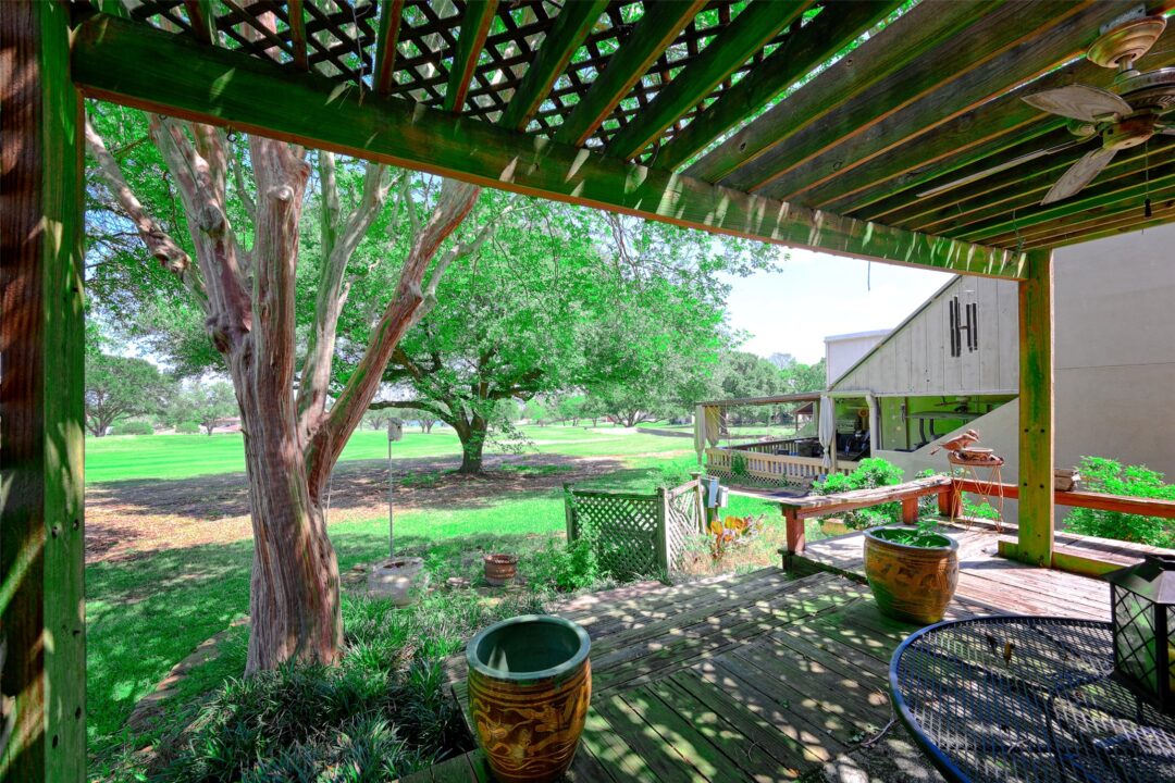 Backyard Patio Under a Green Wooden Pergola with Potted Plants and a View of the Lawn and Trees Beyond