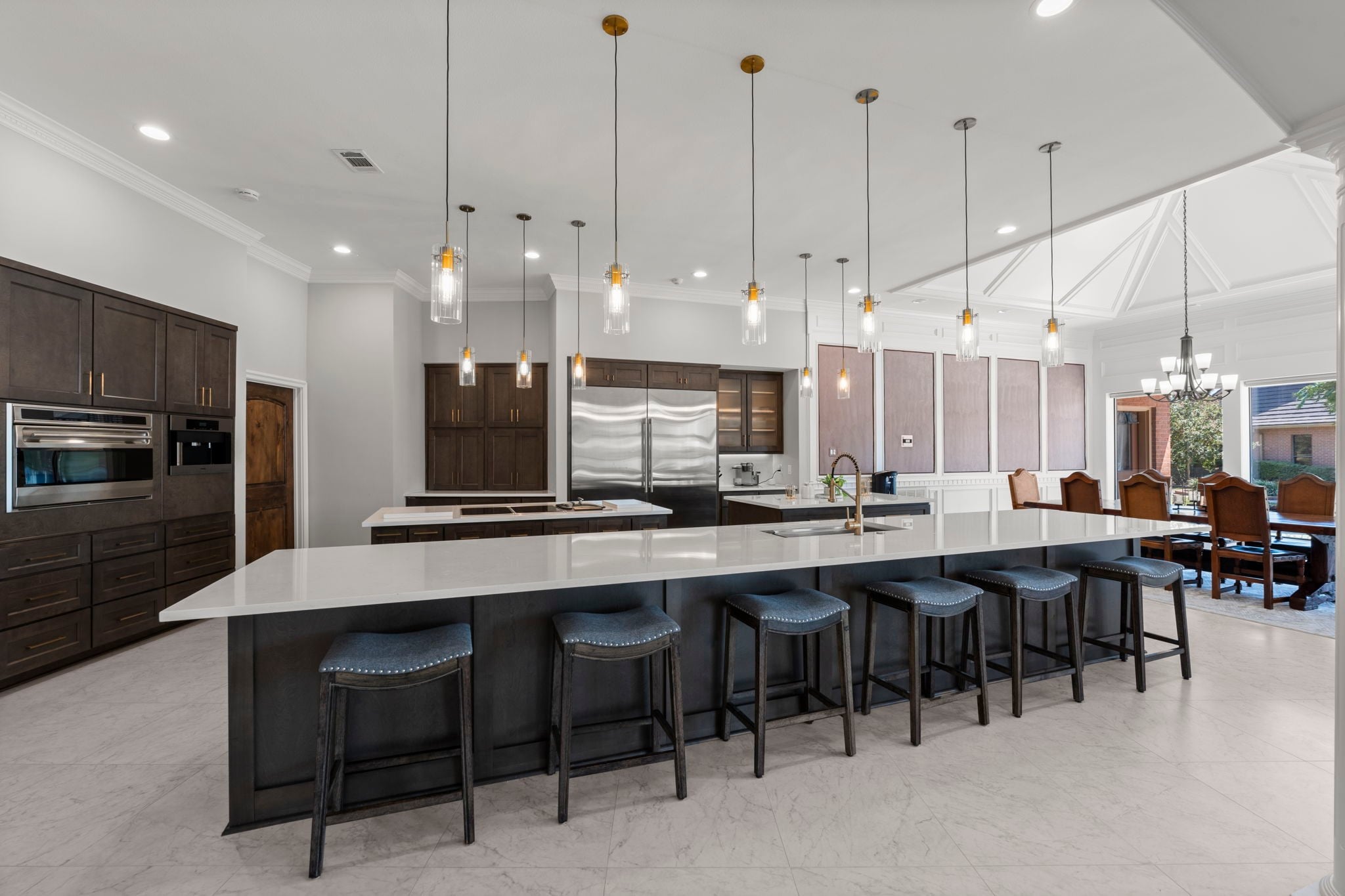 Modern Kitchen with a Large White Island Dark Wood Cabinets and Pendant Lights Above the Counter Stainless Steel Appliances Visible in the Background