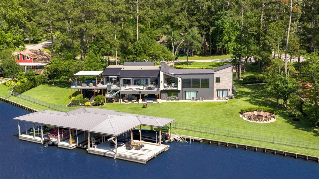 a Modern Lakefront Home with Multiple Terraces a Large Lawn and a Boat Dock Along the Water Underside a Forested Backdrop