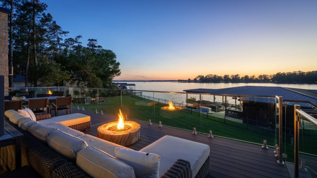 | the mckellar group Sunset View over a Lake from a Modern Deck with Fire Pits and Wicker Seating Glass Railing Surrounds the Patio