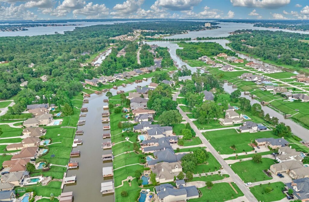 What does a real estate agent do on lake conroe texas | the mckellar group Aerial View of a Flooded Suburban Neighborhood with Water filled Streets and Canal front Homes Boats Docked Along the Water and Green Lawns Surrounding Houses Under a Cloudy Sky