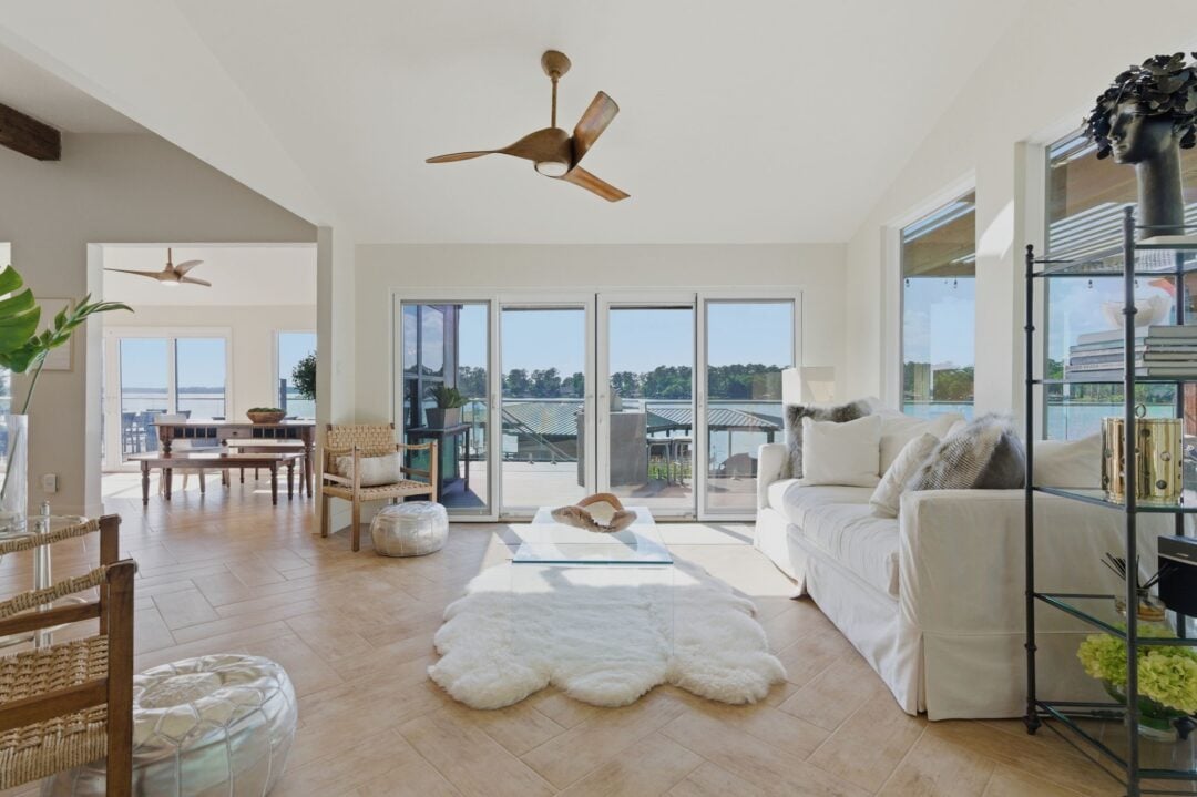 Bright Airy Living Room with Large Glass Doors to a Water View White Sofa and a Wood Ceiling Fan Centerpiece