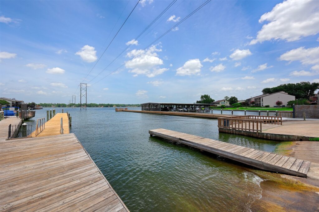 Lake conroe relocation guide for out of state buyers | the mckellar group Waterfront Scene with Wooden Docks Along a Calm River and a Boat Shelter in the Distance Under a Blue Sky with Scattered Clouds