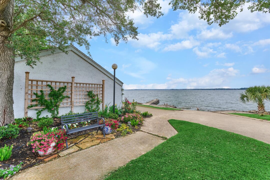 Lakeside Garden with a White Wall Bench Trellis and Colorful Flowers Facing a Calm Lake Under a Blue Sky