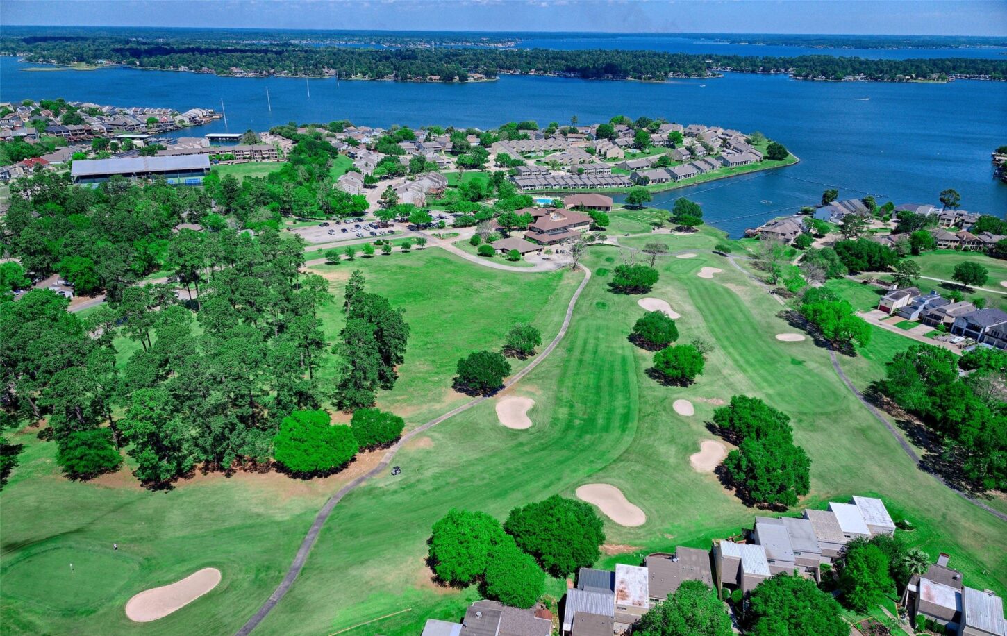 Aerial View of a Green Golf Course Surrounded by Houses and Trees with a Lake in the Background and a Yellow Arrow Marking a Spot Near the Bottom right Corner