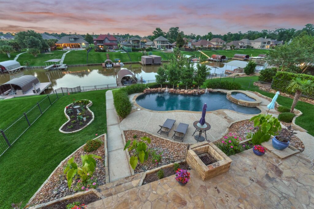 | the mckellar group Backyard Patio with a Curved Pool and Spa Potted Plants and Stone Paths Overlooking a Canal with Boat Docks and Row of Houses at Dusk