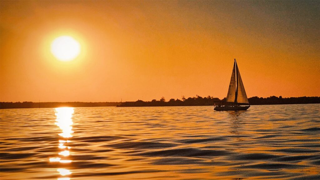 Sailboat Gliding on Orange Sunset lit Lake with the Sun Low on the Horizon to the Left