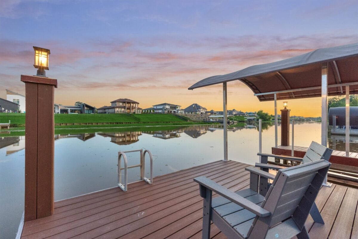 83 083 11452 grand pine dr | the mckellar group Sunset over a Lakeside Neighborhood with a Wooden Dock and Lamp Posts Reflecting on Calm Water Beside a Covered Seating Area with Adirondack Chairs