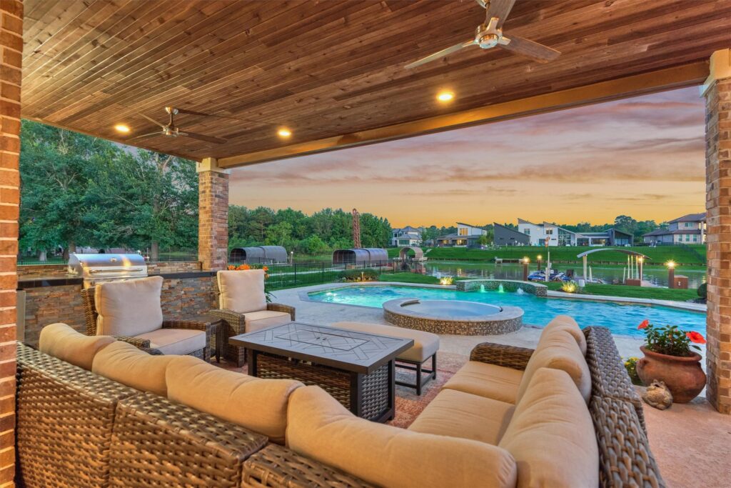 | the mckellar group Covered Patio with Beige Cushioned Wicker Seating and a Coffee Table Overlooking a Pool and Spa at Sunset