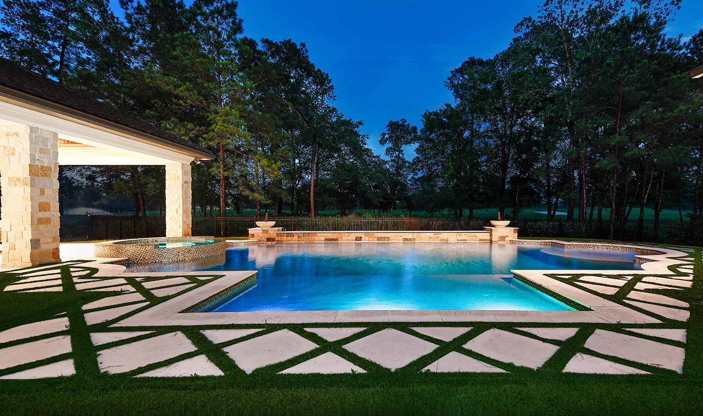 | the mckellar group Luxurious Backyard Pool at Dusk with Blue lit Water Stone Pillars and a Geometric Grass and concrete Inlay Surrounding the Deck