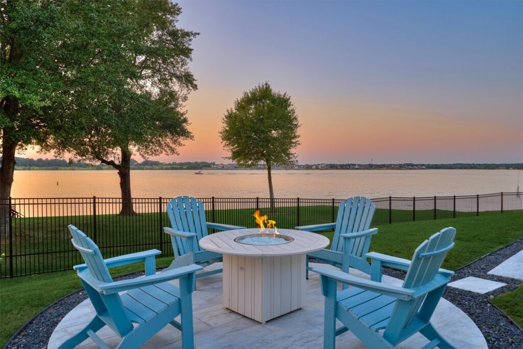 | the mckellar group Blue Adirondack Chairs Surround a Circular Fire Pit on a Stone Patio Overlooking a Lake at Sunset