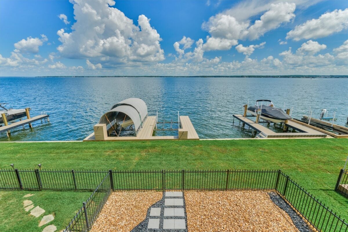 | the mckellar group Lakeside Scene with a Wooden Dock and a Covered Boat Slip a Motorboat on the Right and a Green Lawn in Front