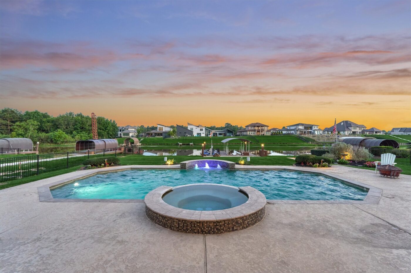 | the mckellar group Resort style Pool with a Circular Hot Tub in the Foreground and a Manicured Lawn Houses and Trees at Sunset in the Background